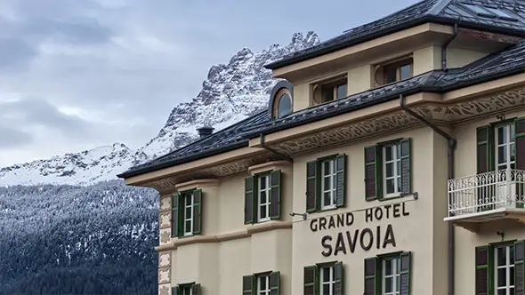 Исторический фасад Grand Hotel Savoia в Кортина-д&rsquo;Ампеццо на фоне заснеженных вершин Доломитовых Альп.