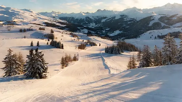 Панорамный вид на заснеженные трассы и горные хребты Мерибеля в Трёх Долинах при мягком зимнем солнце.