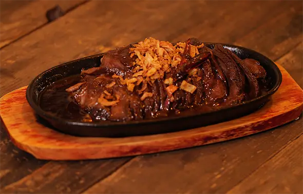 Острое блюдо Basilic Thai (Pad Kra Pao) с говядиной и хрустящим луком на чугунной сковороде.