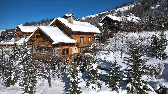 Экстерьер традиционного деревянного шале в Мерибеле, окруженного заснеженными елями под ярко-синим небом
