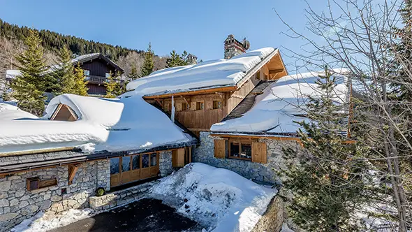 Экстерьер премиального шале в Мерибеле с фасадом из натурального камня и дерева под массивным слоем снега