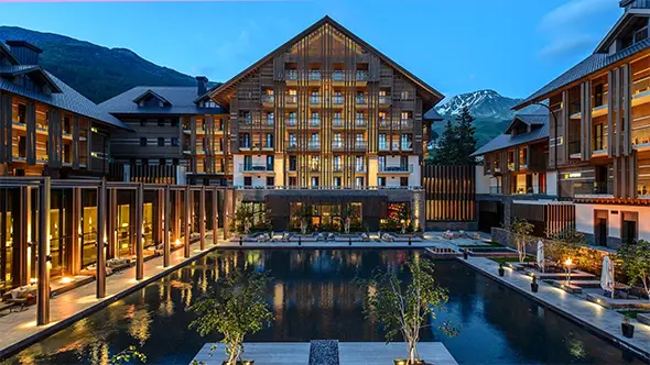 Фасад отеля The Chedi Andermatt в сумерках на фоне заснеженных Альп.