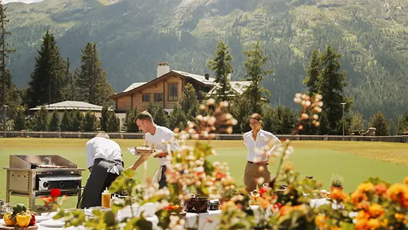 Chefs cooking barbecue outdoors with a hotel in the background.