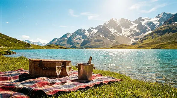 Picnic basket and champagne on the shore of a mountain lake.