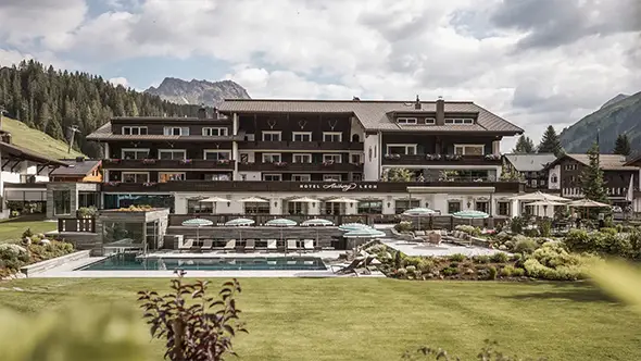 Фасад отеля Hotel Arlberg Lech с бассейном летом.