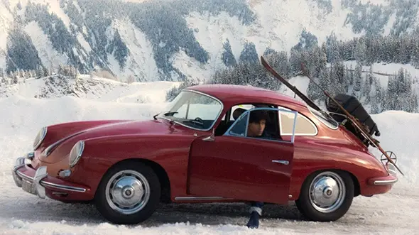 Red vintage Porsche 356 with skis against the snowy mountains.