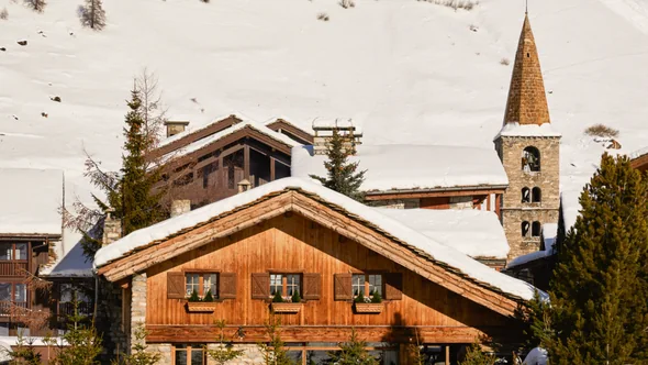 Chalet Schuss under snow beside a stone bell tower in Val d’Isere