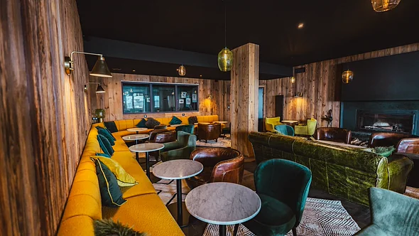 Fireside lounge with yellow banquette, green velvet chairs and an open fire at Fahrenheit Seven Val Thorens