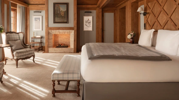Timber-ceilinged bedroom with a fireplace and a checked armchair in Les Chalets des Airelles, Courchevel