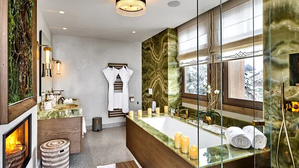 Bathroom in green stone with a bathtub and the double-sided fireplace of Deluxe Room 4, Lys Martagon, Courchevel 1850
