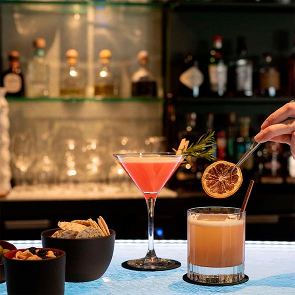 Классический интерьер Bar Annapurna: округлая деревянная барная стойка с красными кожаными стульями, массивный каменный камин с резьбой, зеленое вельветовое кресло и мягкий красный диван.