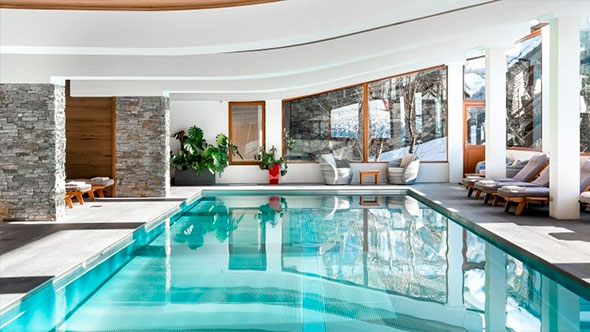 Элегантный крытый бассейн в SPA-центре Hôtel Annapurna с панорамными окнами, открывающими вид на заснеженный Куршевель, и зоной отдыха с шезлонгами, идеально подходит для релаксации после катания.