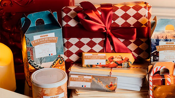 Крупный план праздничных рождественских десертов и шоколадных плиток от Christophe Adam (L’Éclair de Génie), упакованных в тематические коробки с бантами, подчеркивающий высокую кондитерскую кухню отеля Barrière Les Neiges.