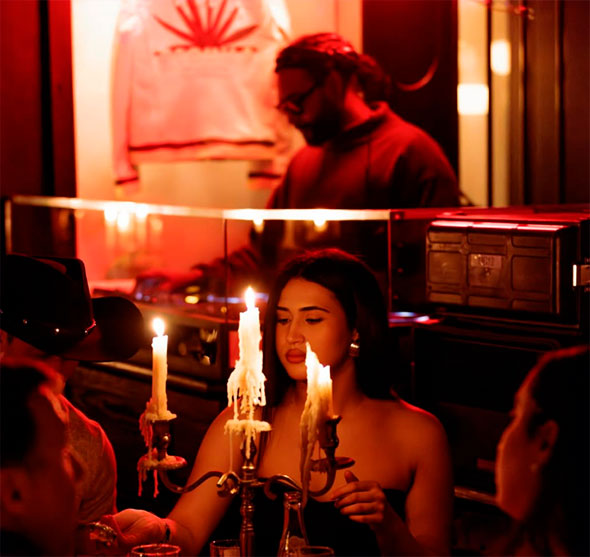 Атмосферное фото интерьера La Mangeoire во время вечеринки: девушка сидит за столом, освещенным тающими свечами в канделябре, а на заднем плане за диджейским пультом работает DJ.