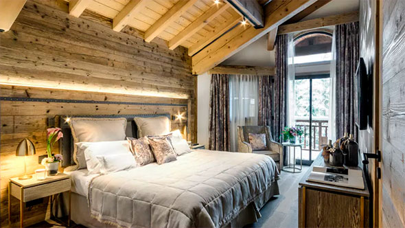 Роскошная спальня в сьюте отеля La Sivoli&egrave;re, выполненная в стиле &laquo;горный шик&raquo; с деревянной отделкой, открытыми балками и большой двуспальной кроватью.