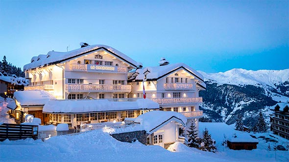 Фасад легендарного пятизвездочного отеля Le Chabichou в Куршевеле, укрытый снегом на фоне альпийских гор. / Exterior of the legendary five-star Le Chabichou hotel in Courchevel, covered in snow against the backdrop of the Alpine mountains.