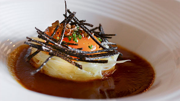 Изысканное блюдо: небольшая горка из мелко нарезанных трав, зелени и мяса/грибов, увенчанная стручком зеленого перца (или огурцом), подается на круглой деревянной тарелке