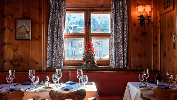 Внешний вид традиционного альпийского здания ресторана Chasellas из камня с деревянными ставнями, расположенного среди заснеженных деревьев в солнечный зимний день. 