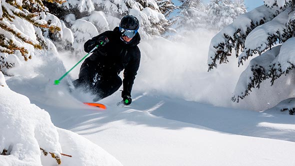Горнолыжник спускается по глубокому свежему снегу среди заснеженных деревьев в Куршевеле. / A skier descending through deep fresh powder among snow-covered trees in Courchevel.