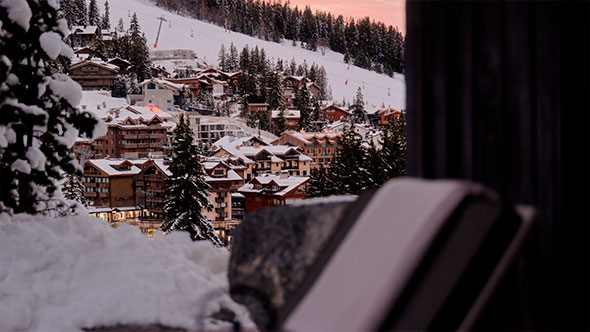 Панорамный вид на заснеженную деревню Куршевель со множеством шале и горнолыжными трассами на склоне горы, снятый с террасы или балкона на закате