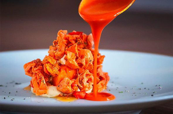 Close-up: Rich red sauce being poured over a dish of crispy orange chips, likely containing lobster or crab.
