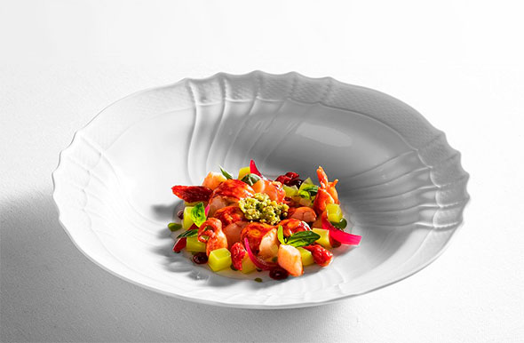 Изысканное блюдо с креветками, фруктами и зеленью, подаваемое в глубокой белой тарелке.