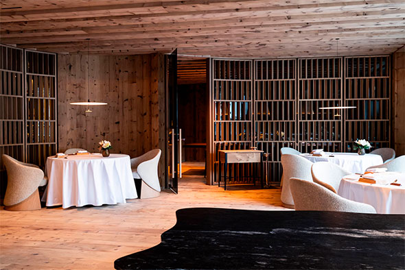 Современный интерьер ресторана с деревянными панелями и полукруглыми перегородками, белые скатерти, мягкие стулья.