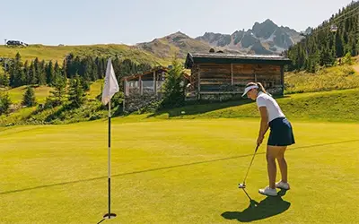 A golf player on a course in Courchevel with mountains in the background.