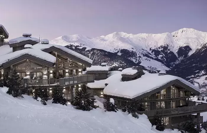 Snow-covered chalet roofs at dusk with the Courchevel peaks behind