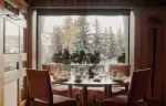 Round table set for dinner before a window onto the snowy pines