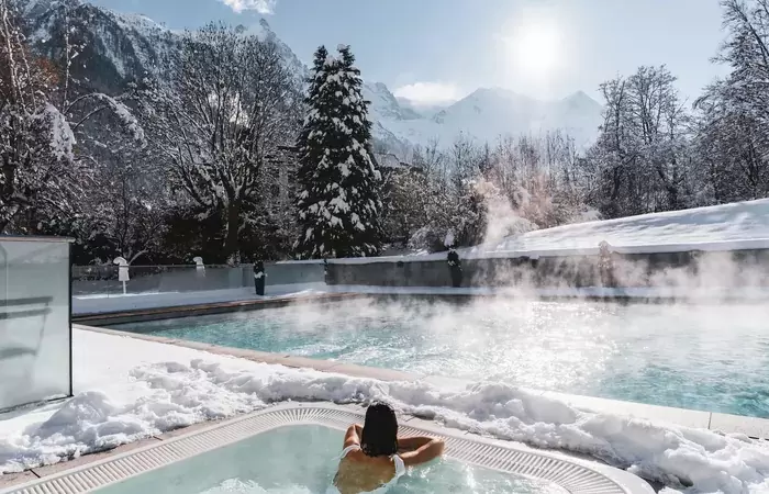 Steaming outdoor pool and hot tub among snowy fir trees at Hotel Mont-Blanc Chamonix