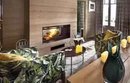 Fireplace in a wooden wall beside leaf-print armchairs in Deluxe Room 4, Lys Martagon, Courchevel 1850